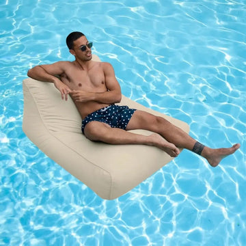 Man lounging on a beige bean bag pool float in a pool