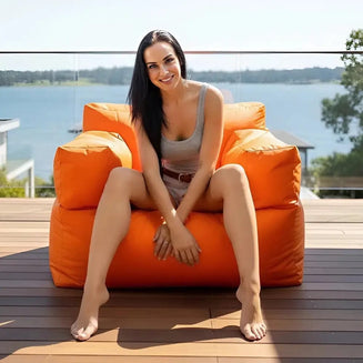Woman sitting on an orange bean bag chair by a lake
