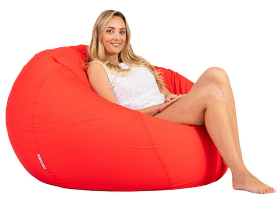 Woman sitting on a large red bean bag chair against a white background